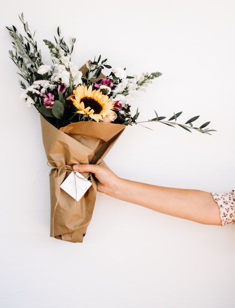 a woman's arm holds a boquet in brown wrapping paper